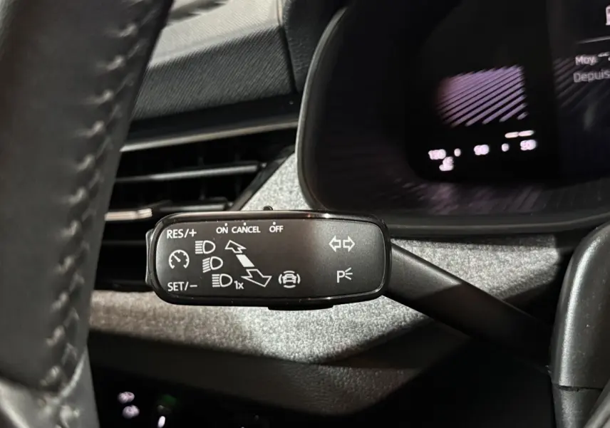 Gros plan sur la commande multifonction côté gauche du volant du Skoda Kamiq rouge 2024, avec affichage digital en arrière-plan.