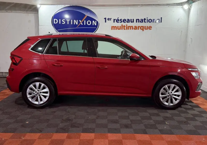 Profil latéral droit d'un Skoda Kamiq rouge 2024, avec jantes alliage et barres de toit noires visibles.
