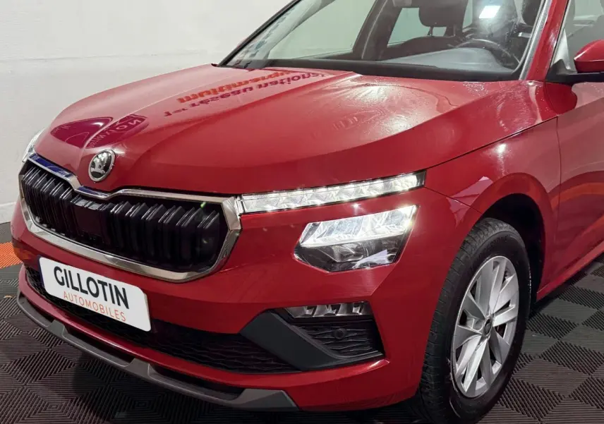 Vue 3/4 avant droite d'un Skoda Kamiq rouge 2024 avec calandre noire et phares LED allumés.