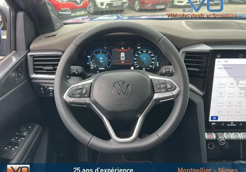 Vue intérieure centrée sur le volant cuir multifonctions d’un Volkswagen Amarok bleu, tableau de bord digital et écran tactile visibles.