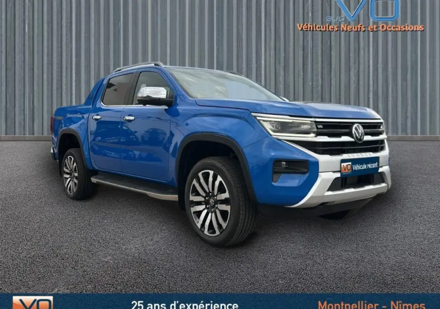 Vue 3/4 avant gauche d’un Volkswagen Amarok bleu 2025 avec jantes alliage 21 pouces et marchepieds visibles.