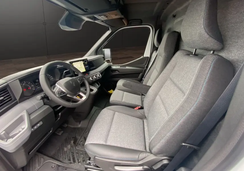 Vue intérieure côté conducteur du Renault Master blanc 2025, sièges tissu gris avec surpiqûres bleues et tableau de bord moderne.