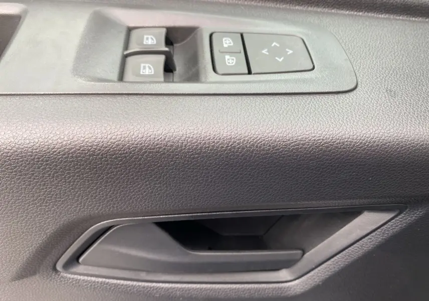Gros plan sur la poignée intérieure et les commandes de vitres électriques côté conducteur du Renault Master blanc.
