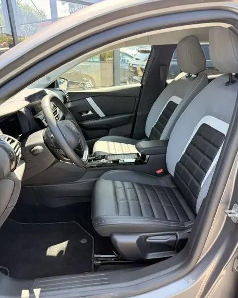 Vue intérieure côté conducteur de la Citroën C4 gris foncé 2025, sièges bi-ton cuir noir et gris avec console centrale.