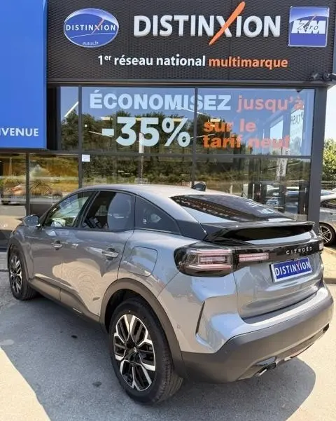 Vue 3/4 arrière droite d'une Citroën C4 gris foncé 2025 avec spoiler de coffre et jantes alliage noires.