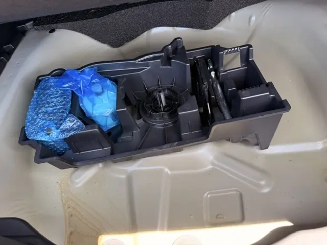 Gros plan sur le rangement sous le coffre d’une Citroën C4 gris foncé, montrant l’emplacement des outils et accessoires.