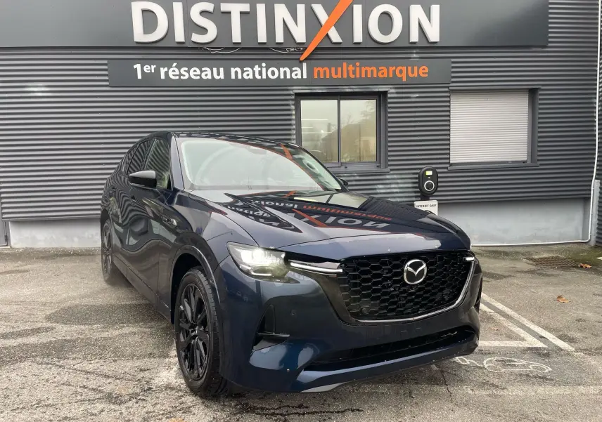 Vue 3/4 avant d'un Mazda CX-60 Deep Crystal Blue avec calandre noire et jantes foncées, stationné devant un bâtiment gris.