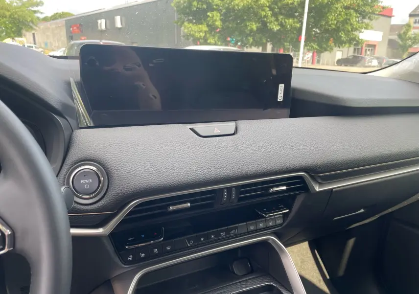 Tableau de bord noir du Mazda CX-60 2024 avec écran tactile large et commandes climatisation visibles côté passager.