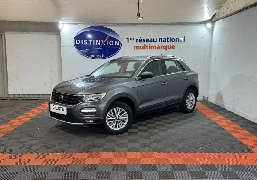 Volkswagen T-Roc gris foncé vue 3/4 avant droit dans un showroom avec sol noir et bandes orange.