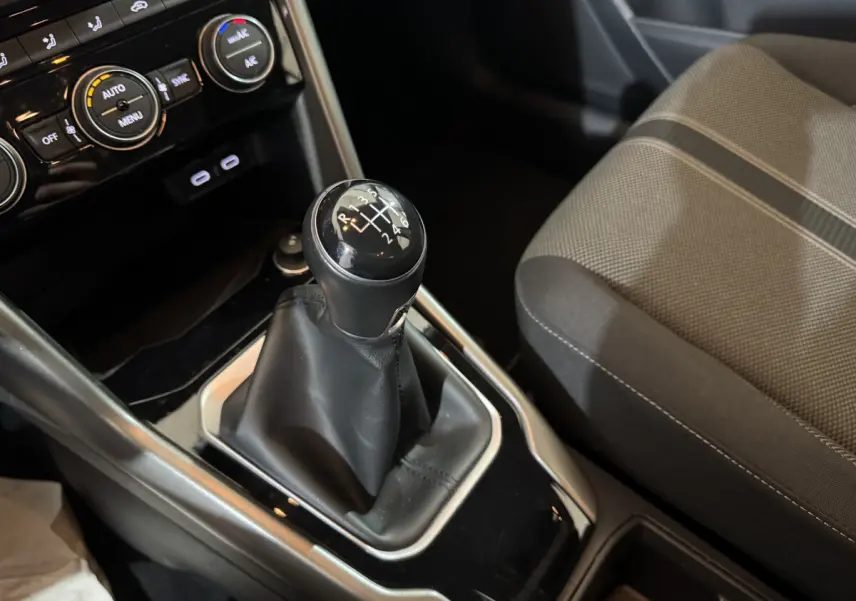 Gros plan sur levier de vitesses manuel et console centrale noire du Volkswagen T-Roc gris foncé, siège tissu à motifs visible à droite.
