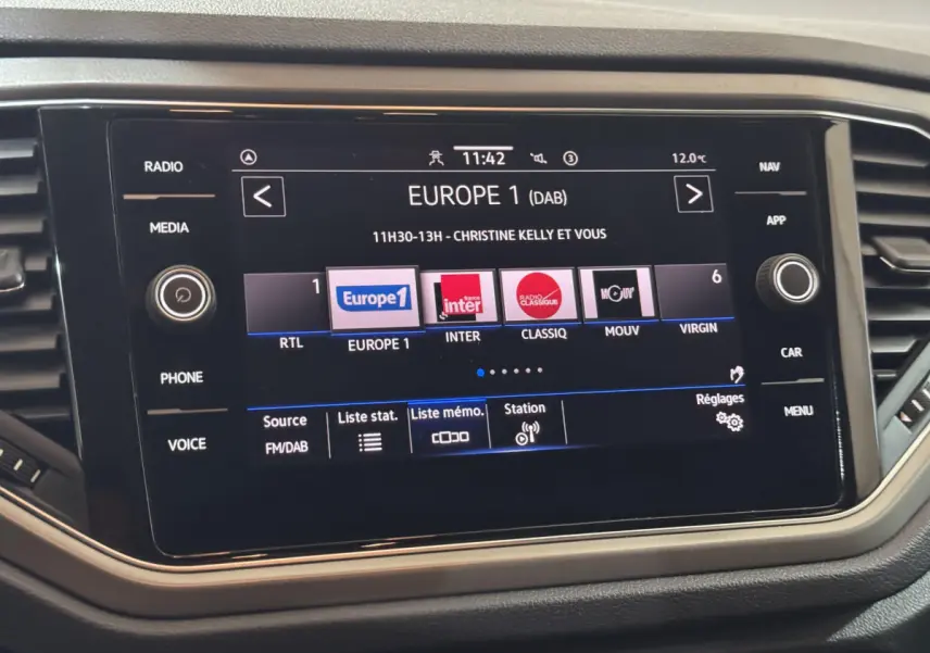 Écran tactile central du tableau de bord du Volkswagen T-Roc 2.0 TDI gris foncé, affichant les stations radio FM/DAB.