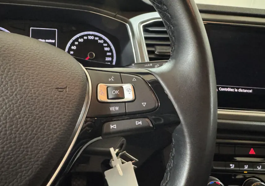 Gros plan sur le volant cuir noir et le tableau de bord digital du Volkswagen T-Roc gris foncé 2021, version Lounge Business.