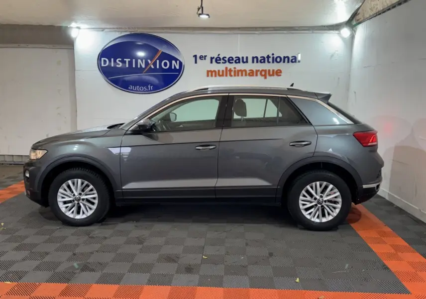 Profil côté gauche d'un Volkswagen T-Roc gris foncé 2021 garé en intérieur avec jantes alliage et toit noir.