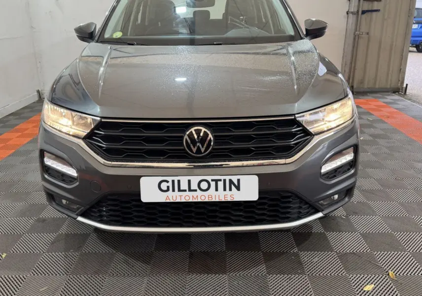 Vue frontale d'un Volkswagen T-Roc gris foncé avec phares allumés et calandre noire hexagonale.