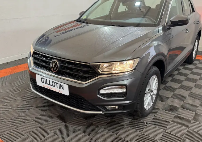 Vue 3/4 avant droit d’un Volkswagen T-Roc gris foncé avec phares allumés et calandre noire distinctive.