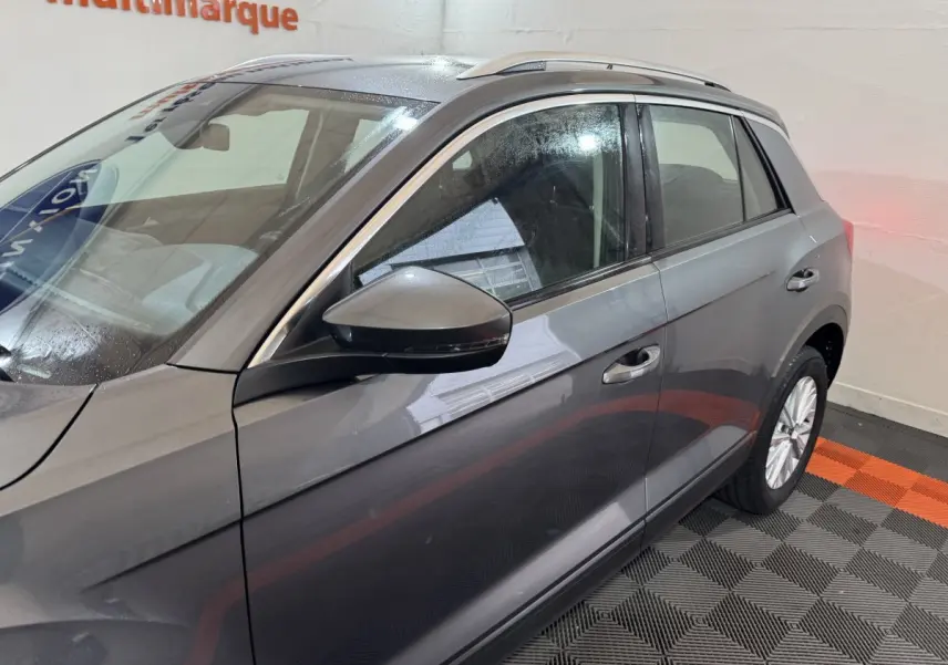 Vue latérale côté gauche du Volkswagen T-Roc gris foncé avec rétroviseur et jante alliage visibles en intérieur showroom.