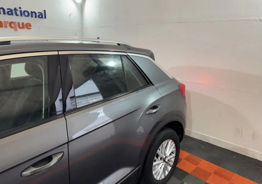 Vue latérale arrière droite d'un Volkswagen T-Roc gris foncé avec jante alliage et barres de toit noires.