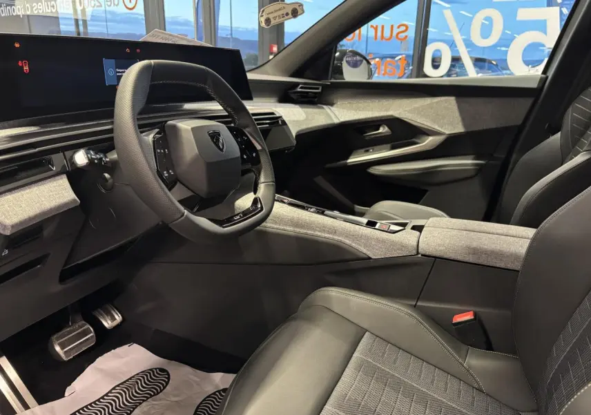 Intérieur avant droit du Peugeot 3008 2025, sellerie tissu gris et cuir, planche de bord avec décor tissu chiné et volant compact noir.