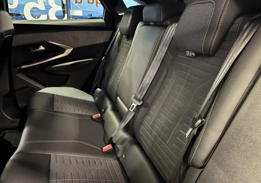 Vue intérieure des sièges arrière en tissu et cuir noir du Peugeot 3008 Hybrid 2025, avec ceinture de sécurité et porte arrière.