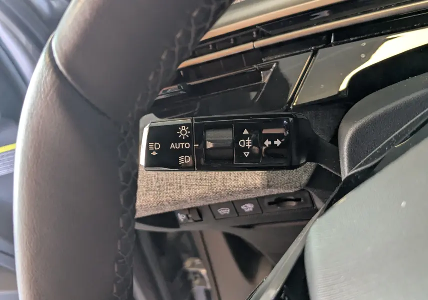 Gros plan sur la commande des feux et clignotants à gauche du volant dans l’habitacle gris du Peugeot 3008 2024 hybride.