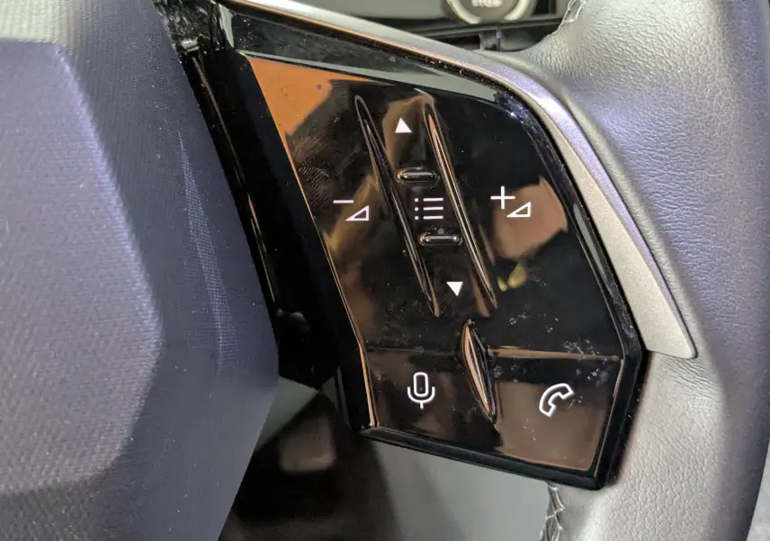 Gros plan sur les commandes noires du volant côté gauche du Peugeot 3008 gris hybride 2024, avec boutons volume et appel.