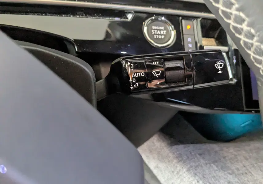 Gros plan sur la commande des essuie-glaces et le bouton start/stop dans l'habitacle noir du Peugeot 3008 gris 2024.