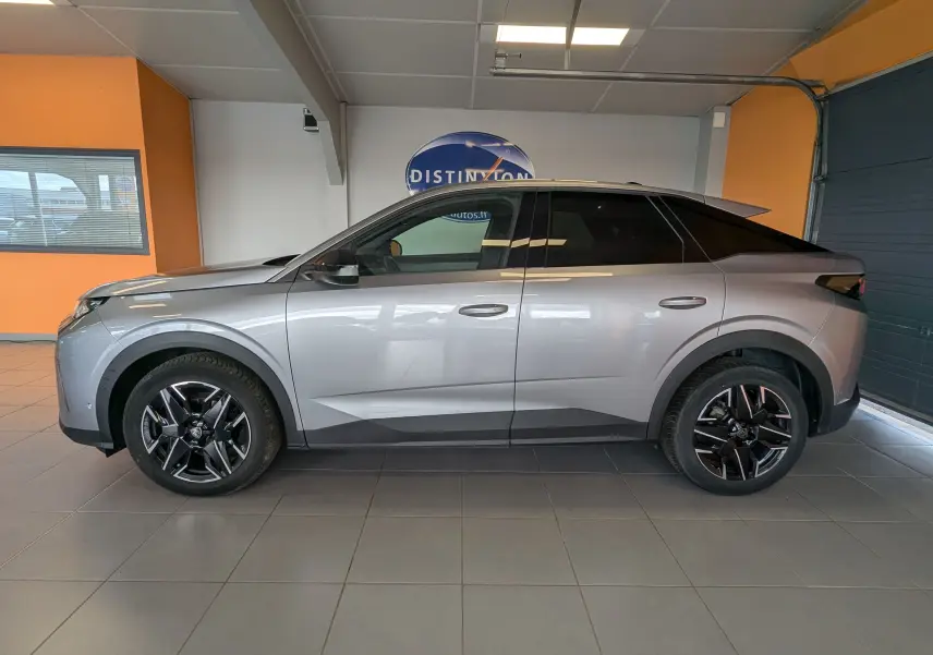 Profil côté gauche d’un Peugeot 3008 gris 2024 hybride essence, avec jantes noires et toit noir en intérieur showroom.