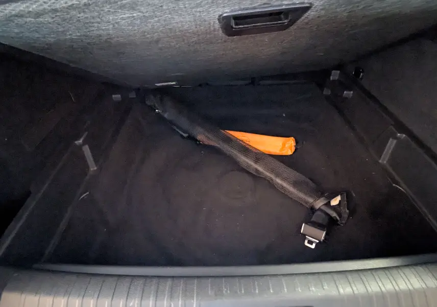 Coffre ouvert d’un Peugeot 3008 gris 2024, vue plongeante sur un espace vide avec un triangle de signalisation orange et un objet noir.
