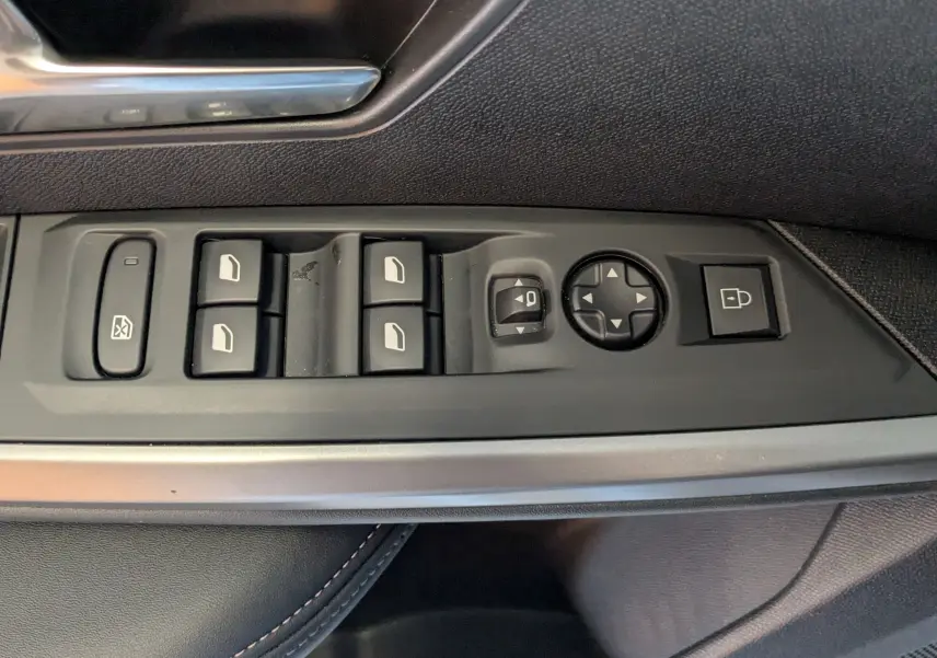 Gros plan sur les commandes des vitres et rétroviseurs côté conducteur d’un Peugeot 3008 gris, version 2024 hybride.