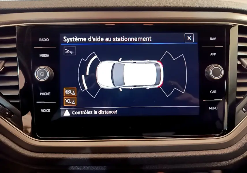 Écran tactile central du Volkswagen T-Roc gris foncé montrant le système d'aide au stationnement en vue de dessus du véhicule.