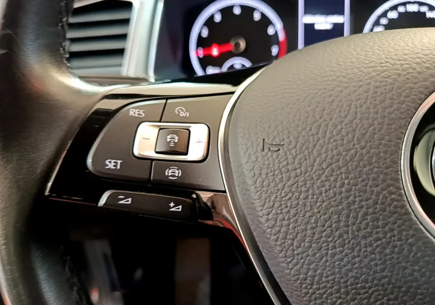 Gros plan sur le volant cuir du Volkswagen T-Roc 2021, montrant les commandes multifonctions côté gauche et le tableau de bord flou.