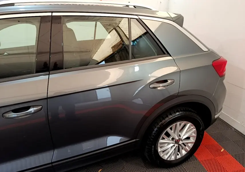 Vue latérale côté droit du Volkswagen T-Roc gris foncé, mettant en valeur la roue arrière et les vitres teintées.