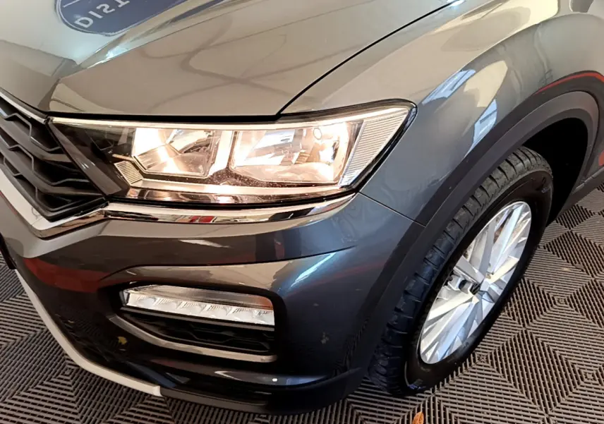 Gros plan sur l'avant droit gris foncé du Volkswagen T-Roc 1.0 TSI avec phares et feux antibrouillard visibles.