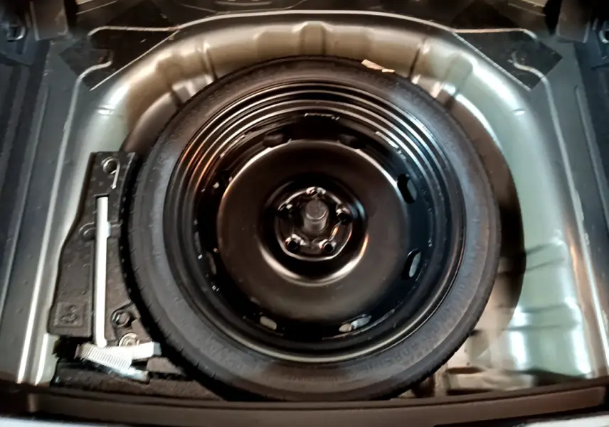 Roue de secours noire dans le coffre d'un Volkswagen T-Roc gris foncé, vue plongeante sur l'espace de rangement.