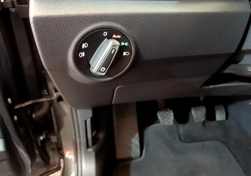 Gros plan sur le tableau de bord côté gauche du Volkswagen T-Roc gris foncé, montrant la commande des phares et les pédales.