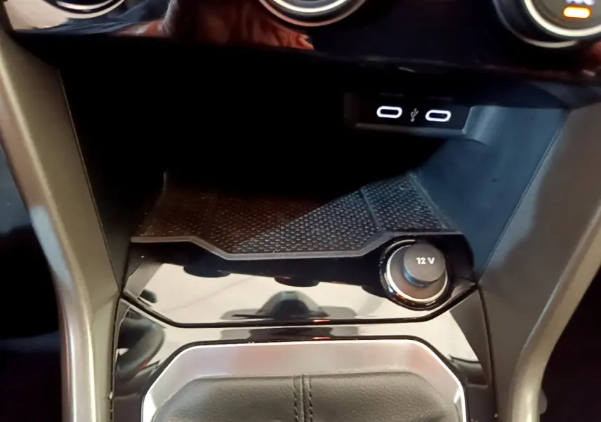 Gros plan sur la console centrale du Volkswagen T-Roc gris foncé, montrant prise 12V et ports USB éclairés.