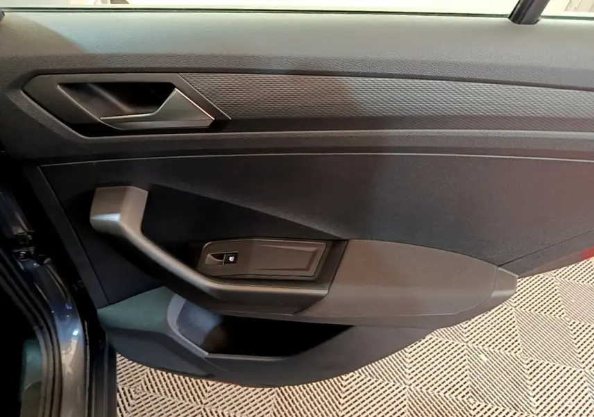 Vue rapprochée de la porte côté conducteur du Volkswagen T-Roc gris foncé, avec poignée et commande de vitre électrique.