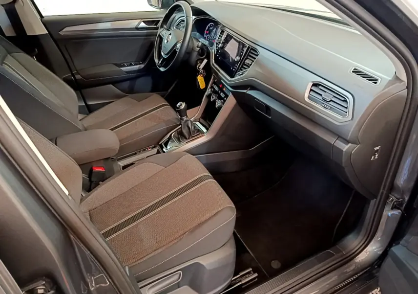 Intérieur avant droit du Volkswagen T-Roc gris foncé 2021, avec tableau de bord moderne et sièges tissu gris.