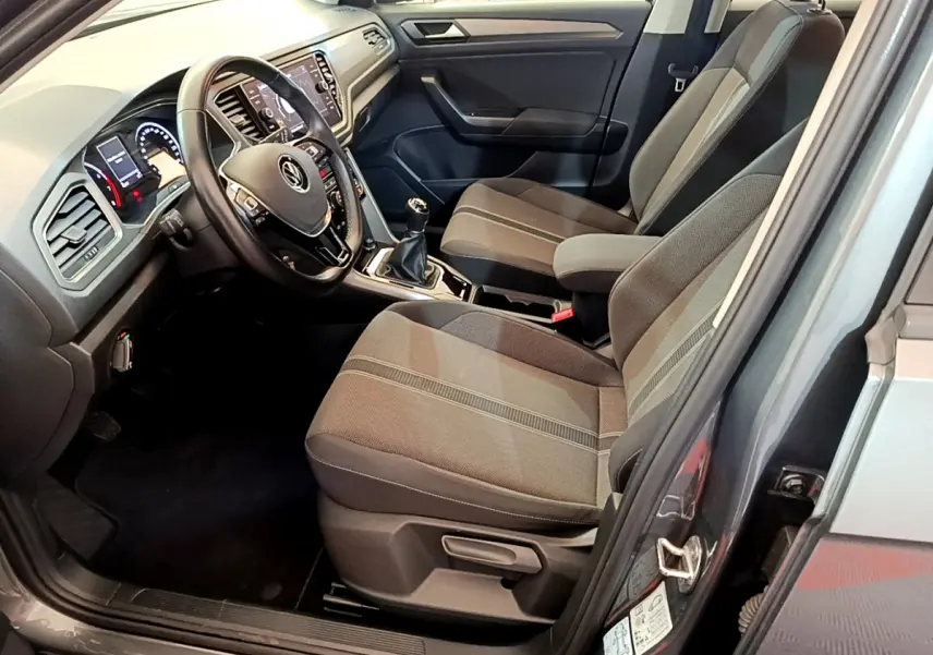 Intérieur du Volkswagen T-Roc gris foncé, vue côté conducteur, sièges tissu et tableau de bord avec écran tactile.