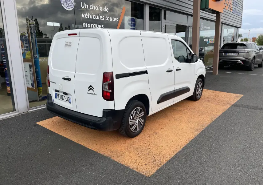 Vue 3/4 arrière droite d'un utilitaire blanc Citroën Berlingo 2018 stationné devant un bâtiment commercial.