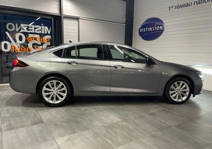 Vue latérale droite d'une Opel Insignia Grand Sport gris clair en showroom avec jantes alliage 17 pouces.