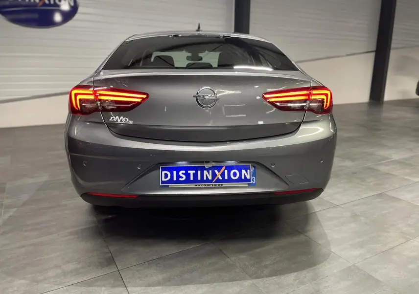 Vue arrière d'une Opel Insignia Grand Sport gris clair avec feux arrière LED allumés dans un showroom.