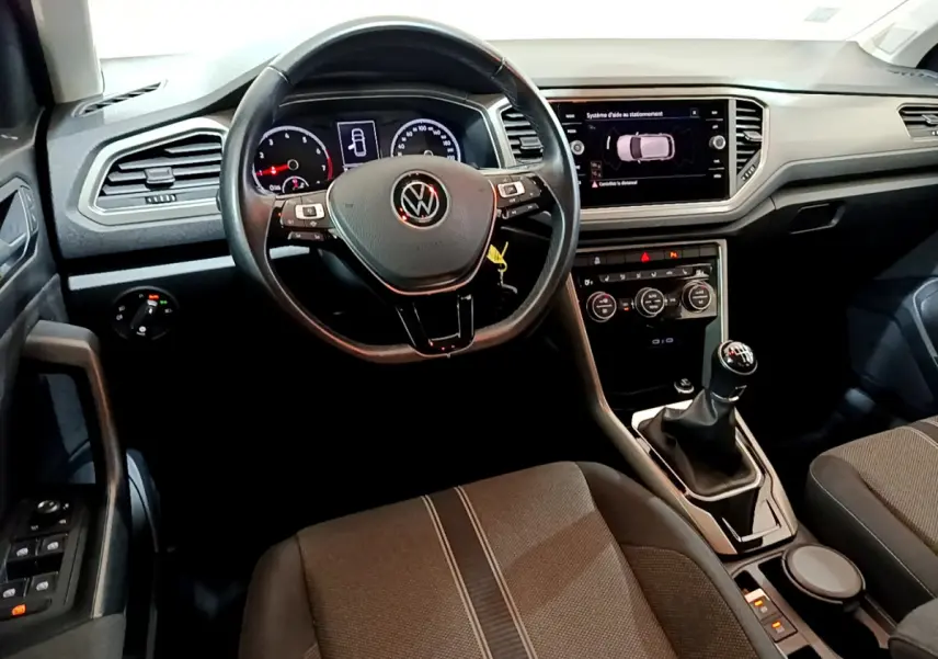 Vue intérieure du poste de conduite du Volkswagen T-Roc 1.0 TSI 110 Lounge avec volant cuir et boîte manuelle.