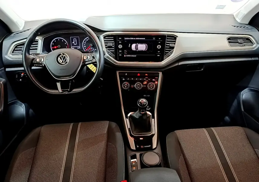Vue intérieure avant du Volkswagen T-Roc 1.0 TSI 110 Lounge 2021, volant cuir et écran tactile central allumé.