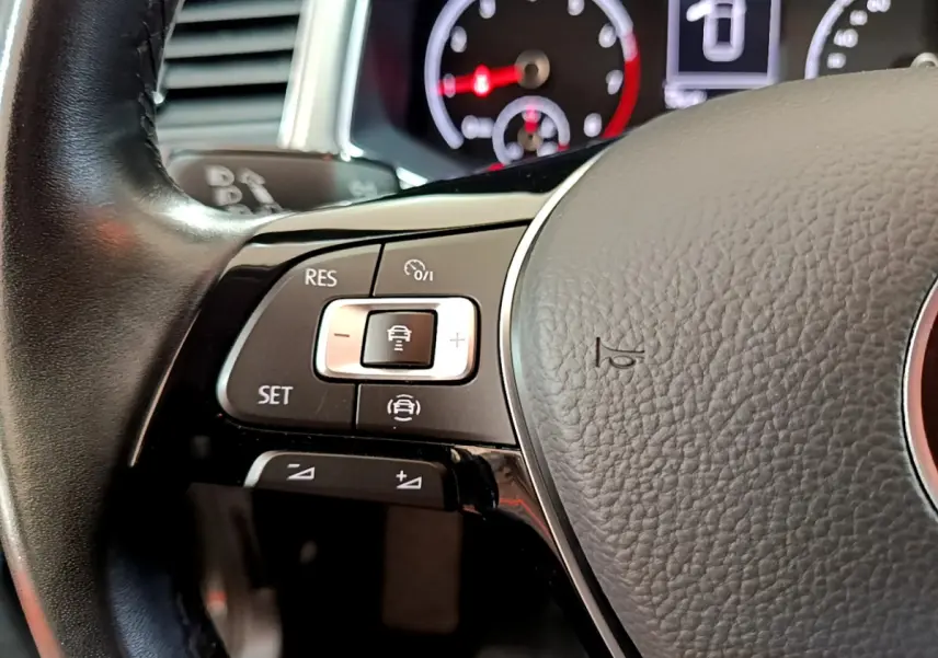 Gros plan sur les commandes du volant cuir du Volkswagen T-Roc 1.0 TSI 110 Lounge, avec tableau de bord en arrière-plan.