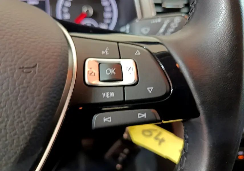 Gros plan sur les commandes gauche du volant cuir noir du Volkswagen T-Roc gris foncé, avec tableau de bord en arrière-plan flou.