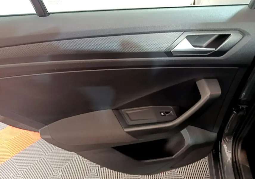 Vue intérieure du panneau de porte côté conducteur du Volkswagen T-Roc gris foncé, avec poignée et commande de vitre électrique.