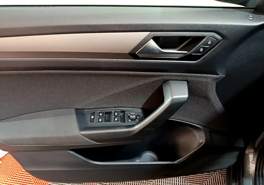 Vue rapprochée de la porte côté conducteur du Volkswagen T-Roc gris foncé, avec commandes électriques et poignée noire.