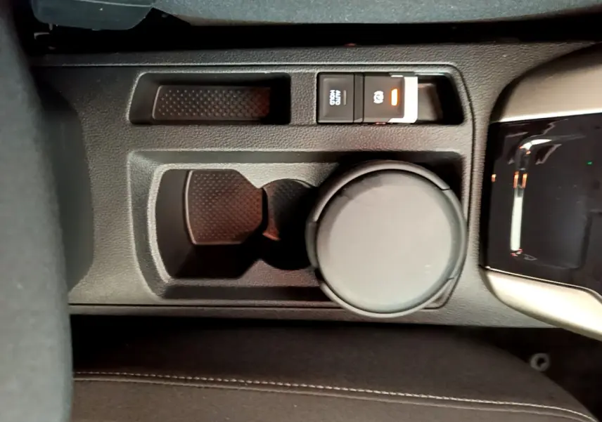 Gros plan sur la console centrale noire du Volkswagen T-Roc 1.0 TSI 110 Lounge avec frein à main électrique et porte-gobelet.