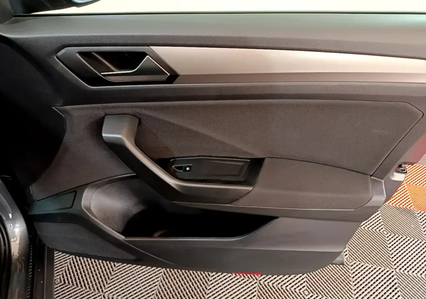Vue rapprochée de la porte intérieure côté conducteur du Volkswagen T-Roc gris foncé avec poignée noire et garniture tissu.